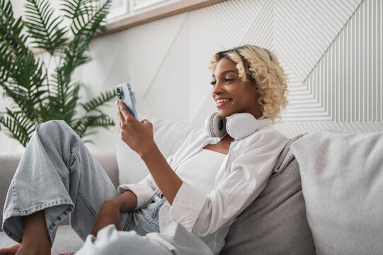 Side view on happy young student african american girl at home using phone for downloding study materials,e-learning,listening to podcast,music,watching videos,online confrences,streaning services etc