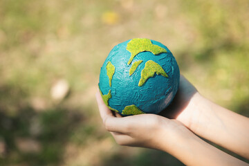 Young boy's hand holding planet Earth globe at natural park background as Earth day to save this planet with ESG principle and environment friendly energy for brighter future. Gyre