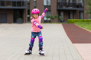 Little cute girl rollerblading in protection, helmet in the city in summer, autumn. Child roller...