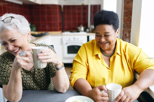 Friendship for life. Retired female friends of diverse ethnicity drinking coffee together after long time no seeing each other, laughing out loud at joke or situation, sharing stories and news