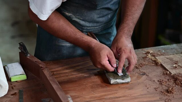 Woodworker is shown sharpening a chisel on a whetstone for making a classical guitar using tools in a traditional