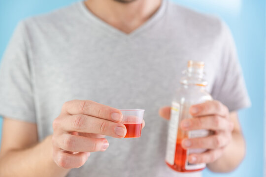 Man holding portion of liquid medicine syrup for treatment cold and flu in measuring cup. Male drinking liquid drug from meds bottle. Taking medicine, health care, pharmacy concept