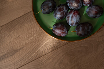 Fresh purple ripe plums on a green plate, close-up. Harvest. Fiber