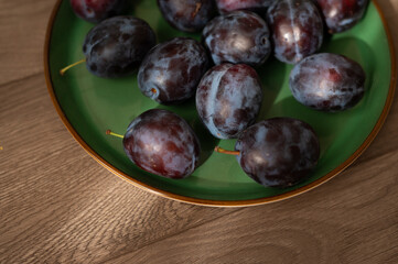 Fresh purple ripe plums on a green plate, close-up. Harvest. Fiber
