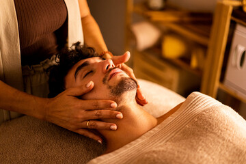 A young adult is lying on a table with his eyes closed receiving a facial massage in a beauty center. Men taking care of their faces. Facial maxophylaxis