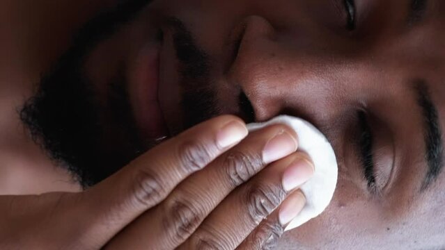 Vertical video. Man care. Face hygiene. Confident satisfied metrosexual guy cleansing cheeks facial skin applying skincare tonic with cotton pad.