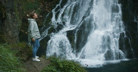 Woman traveler enjoying waterfall in the highlands of Austria. Traveling in the mountains. Girl contemplates the beauty of nature.