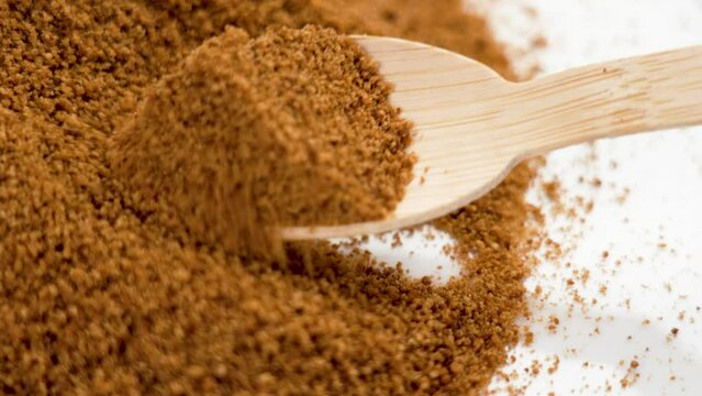 Measuring a portion of brown coconut sugar with a bamboo teaspoon close up to prepare a sweet drink