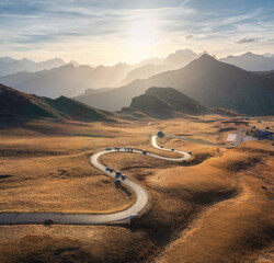 Aerial view of winding road in mountain pass, golden sunlight at sunset in autumn. Passo Giau,...