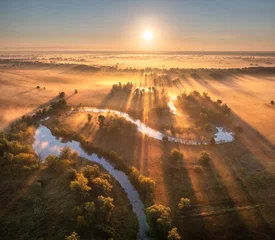 Fotobehang Aerial view of beautiful curving river in low clouds at sunrise in autumn in Ukraine. Turns of river, meadows and fields, grass, orange trees, golden sun rays at dawn in fall. Top view of river coast © den-belitsky