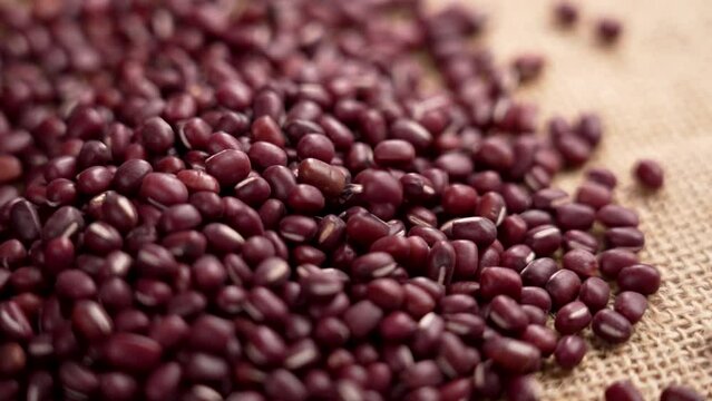 Red Azuki beans on rough burlap falling in slow motion. Raw uncooked Adzuki grains. Vigna angularis. Rotation