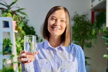 Portrait of smiling young woman with glass of water posing at home