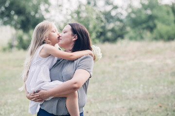 Mom holds her daughter in her arms, plays, kisses her. - obrazy, fototapety, plakaty