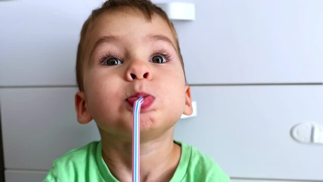 Adorable face of a Caucasian toddler holding a plastic straw in his mouth. Baby boy drinking from a straw. Close up. Vertical screen.