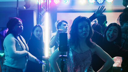 Young adult filming video at party, using mobile phone to record vlog of group of people having fun...