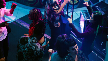 Young people doing funky dance moves on dance floor, enjoying nightlife with electronic music at club. Happy group of friends dancing and partying, having fun at nightclub. Handheld shot.