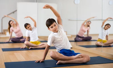 Rucksack Smiling sporty tween boy doing stretching exercises while sitting in lotus position during training with family in fitness center © JackF