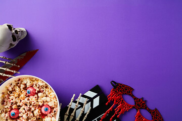 Scary movie night concept. Halloween decorations, clapperboard, bowl of popcorn on purple background.