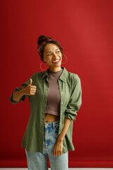Positive woman showin thumbs up with smile while standing over red studio background