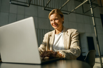 Female sales manager working on laptop while sitting the desk in modern coworking 