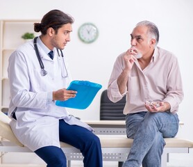 Young male doctor and old patient in antismoking concept