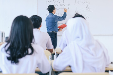 Young Asian teacher teaching in front of classroom while group of multiethnic students listening