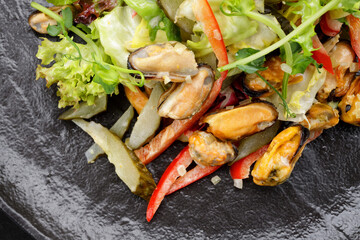 Salad with mussels, on a black plate