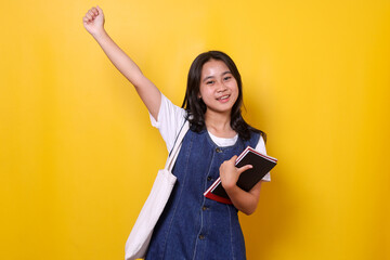 Young beautiful Asia student girl feel free, gesturing celebration over yellow background.