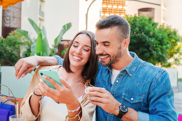 Smiling young couple using a smartphone chatting online on social media and enjoying together. Beautiful girlfriend showing apps to her boyfriend with a cellphone. Partners browsing with mobile phone