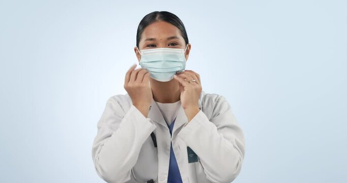 Doctor, face mask and tutorial of woman with thumbs up for covid and disease safety in studio. How to, healthcare and medical professional with portrait and care with protection and blue background
