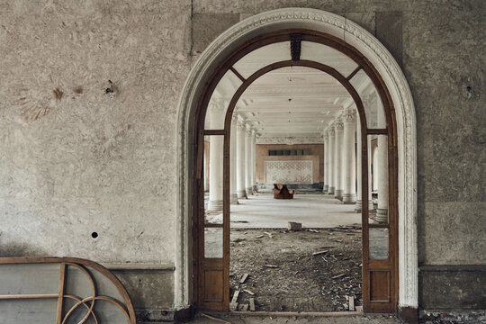 Abandoned soviet spa resort (sanatorium) Shakhter (Miner), in Tskaltubo, Georgia. View of the hall with columns, an old chair in the center. Broken arched door

