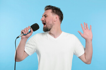 Handsome man with microphone singing on light blue background