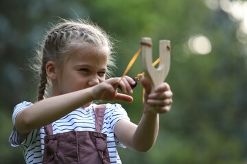 Little girl playing with slingshot in park - obrazy, fototapety, plakaty