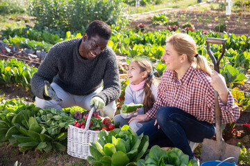 Portrait of happy cheerful couple of farmers with daughter sitting outdoors and smiling at the farm