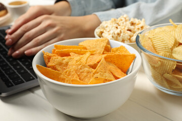 Bad eating habits. Woman working on laptop at white wooden table with different snacks, selective focus