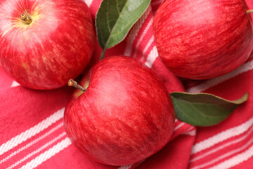Fresh red apples with leaves on red cloth, flat lay