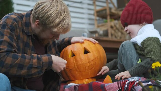 father and son carve Halloween pumpkin while sitting on terrace
