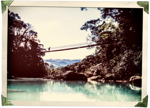 Vintage style adventure travel photo with person crossing a wooden bridge in old photo corners and edges isolated