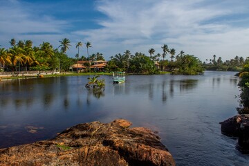 Obraz premium View of the Imbassai River with a boat sailing and reddish rocks, paradisiacal village, on the coast of Bahia, Brazil, near Salvador and Praia do Forte