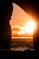 vertical photo of a cave, inside you can see a sunset on the beach.