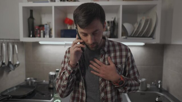 Unhappy male makes phone call requesting some advice in troubled relationship in his kitchen apartment. Sad man discusses private matters by phone with girlfriend in evening at home. Mental problems. 