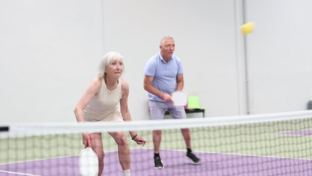 Two pickleball players prepare to return a ball on a pickleball court indoor