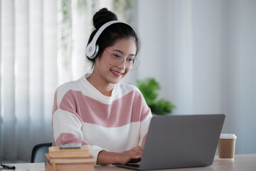 Asian student wearing headphones talking on online chat meeting using laptop in university campus or at virtual office. College female student learning remotely.