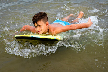 Preteen beach boy having fun riding his boogie board in the ocean waves
