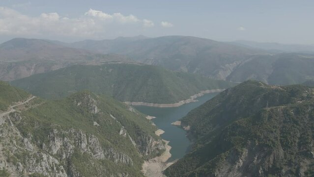 Drone shot flying over the mountains near the Koman lake in Albania on a sunny day with clouds with blue water and a green valley LOG