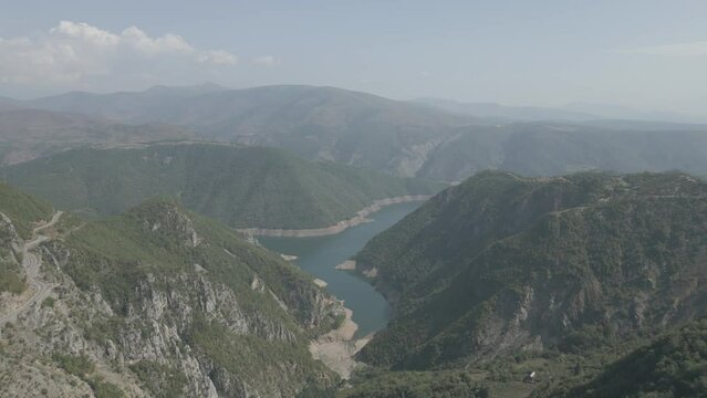 Drone shot flying over the mountains near the Koman lake in Albania on a sunny day with clouds with blue water and a green valley LOG