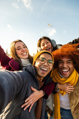 Selfie of multiracial happy friends enjoying winter day outdoors. Happy people looking at camera. Vertical. Copy space. - obrazy, fototapety, plakaty