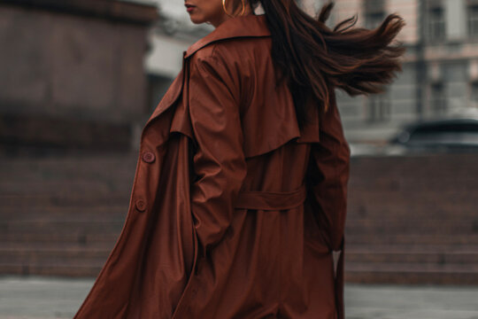 Fancy details of autumn long brown leather trench coat. Street style casual clothing. Woman walking alone in the city.