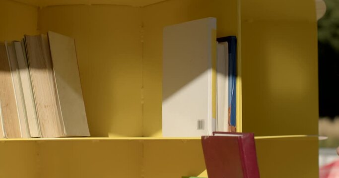 Student takes a book on yellow shelf in open library close up. Environment conducive to academic growth, providing students with easy access to textbooks, reference materials, and study resources.