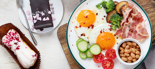 Traditional Englis breakfast plate with bacon strips, sunny side up eggs, vegetables and cake on light background